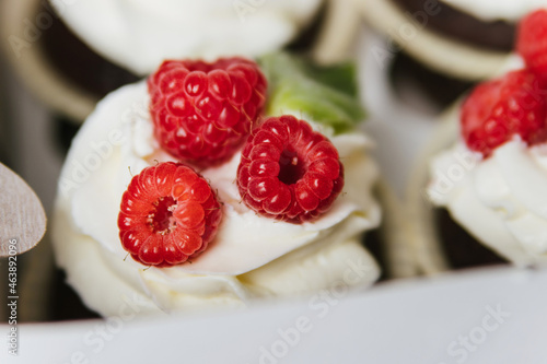 Cupcakes with white butter cream and berries lie in a box.
