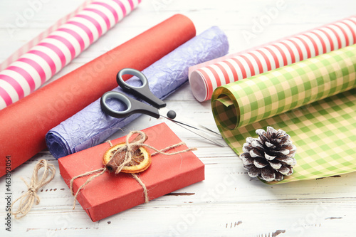 Rolls of craft papers with gift box and scissors on white wooden background