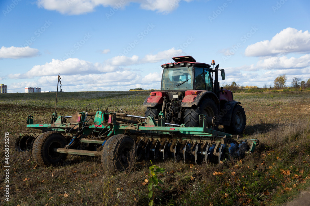 Fototapeta premium A farmer in a tractor, agricultural machinery, prepares the land with a cultivator. A modern red tractor in a field. Plowing a heavy tractor while cultivating agricultural work in a field with a plow.