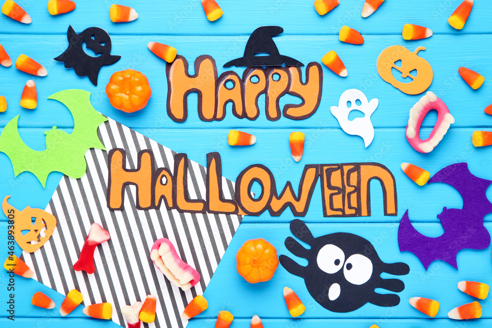 Text Happy Halloween with candies, gelatin, paper bats, ghosts on blue wooden background