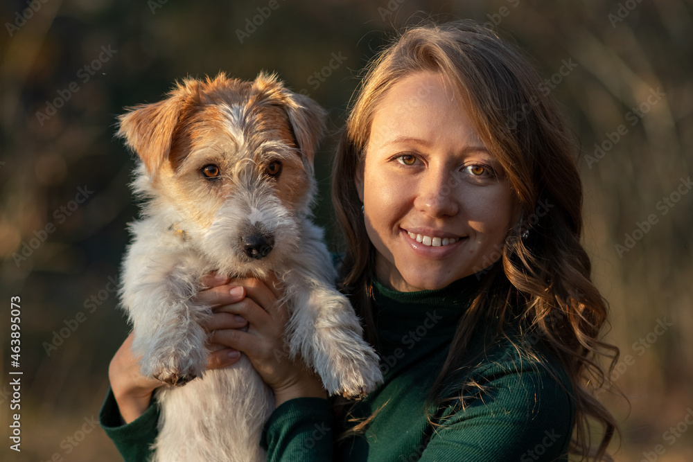 Portrait of a Wire-haired Jack Russell Terrier puppy and a girl in a green dress in an autumn park Portrait of a Wire-haired Jack Russell Terrier puppy and a girl in a green dress in an autumn park