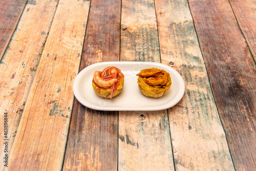 Patacones stuffed with shredded chicken meat and prawns with red onion on wooden table