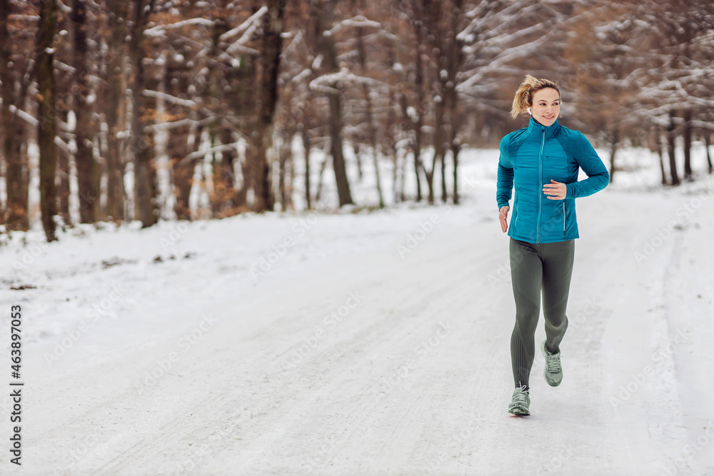 Slim sportswoman jogging in forest on a snowy weather. Cold weather, snow, healthy life, fitness, healthy habits, nature