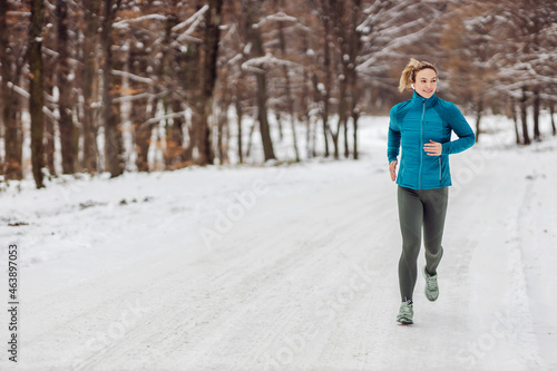 Slim sportswoman jogging in forest on a snowy weather. Cold weather, snow, healthy life, fitness, healthy habits, nature