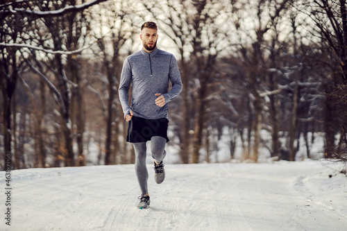 Fit sportsman running in forest at snowy winter day. Winter fitness, snowy weather, healthy habits