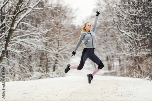Happy sportswoman jumping on snowy path at winter. Healthy life, winter sport, freedom