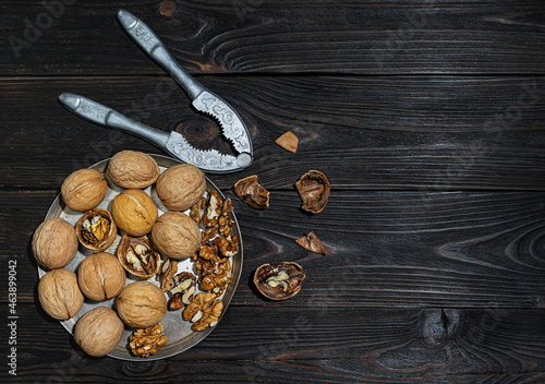 Whole ripe walnuts lie on an iron plate. Nut shells and nutcrackers on dark wooden boards