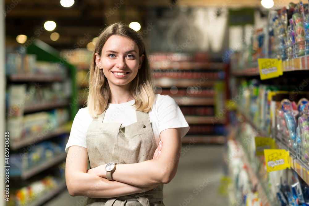 portrait of saleswoman, woman smiling and looking at camera in supermarket.  Pleasant friendly female seller standing in the store between the rows .  Trade business and people concept Photos | Adobe Stock