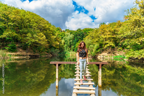 A young woman on a wooden ladder bridge on a forest mountain lake. Amazing summer landscape with a lake and a panoramic view of a mountain lake © KseniaJoyg