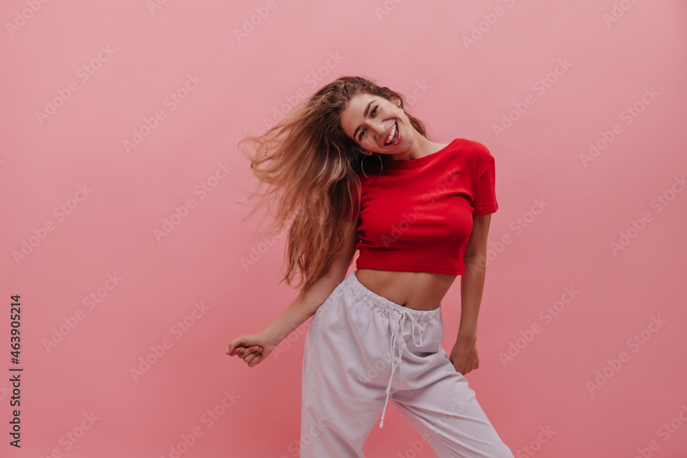 Fabulous russian young girl moves energetically and develops her hair on pink background. Slender blonde with gorgeous smile and good skin poses in home clothes. Concept of enjoying weekend, vacation Fabulous russian young girl moves energetically and develops her hair on pink background. Slender blonde with gorgeous smile and good skin poses in home clothes. Concept of enjoying weekend, vacation