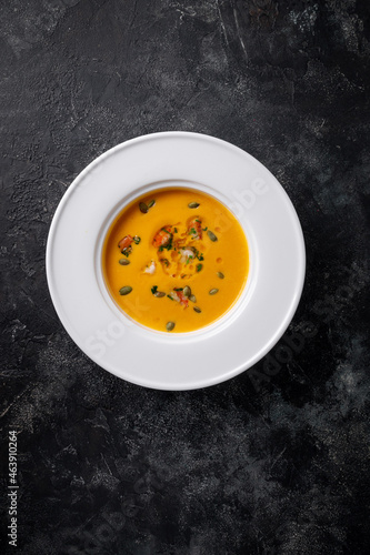 Pumpkin cream soup pureed in a white plate on a dark stone table