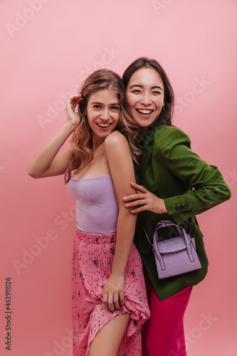 Fototapeta Fashionable young interracial stepsisters laughing in front of camera on pink background