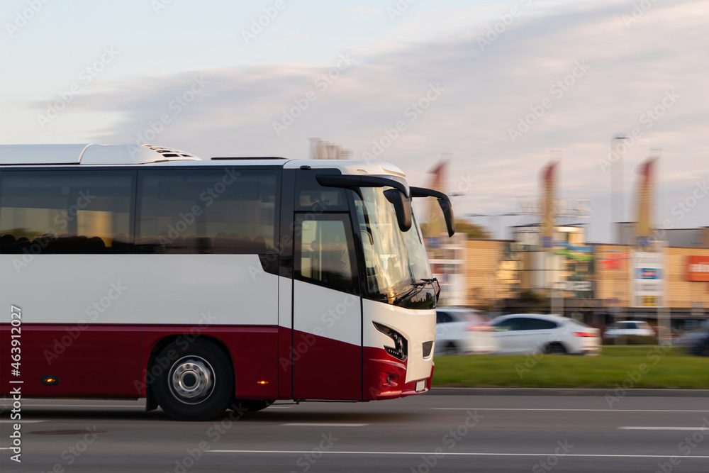 A red-and-white passenger bus travels down the street in close-up. Urban and interurban passenger transport. Motion blur