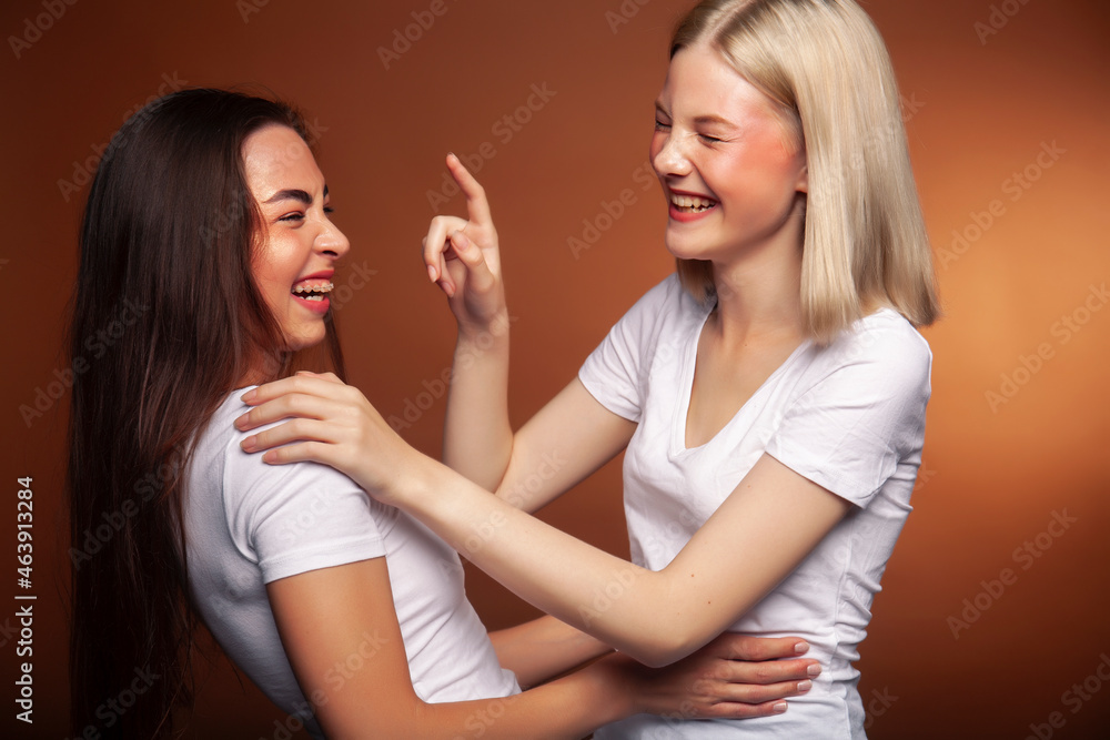 two pretty diverse girls happy posing together: blond and brunette, caucasian and asian on brown background, lifestyle people concept two pretty diverse girls happy posing together: blond and brunette, caucasian and asian on brown background, lifestyle people concept