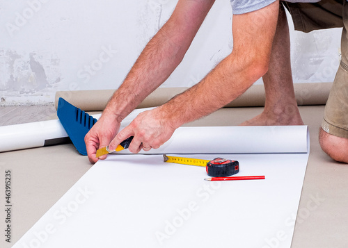 Male hands, the worker measures and cuts the wallpaper to the desired size. Apartment renovation.