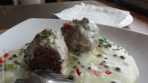 Adding potatoes to a plate with meatballs and white sauce. Traditional German food Koenigsberger Klopse. photo