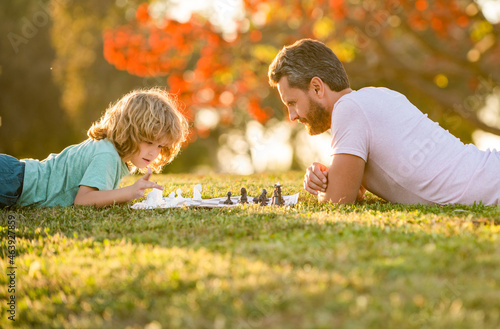happy family of daddy and son kid playing chess on green grass in park outdoor, playing chess