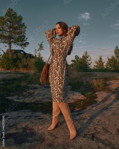 Elegant woman in green dress and high boots wearing green dress and posing at stone outdoors against blue sky. Pretty caucasian female model with long straight hair photo