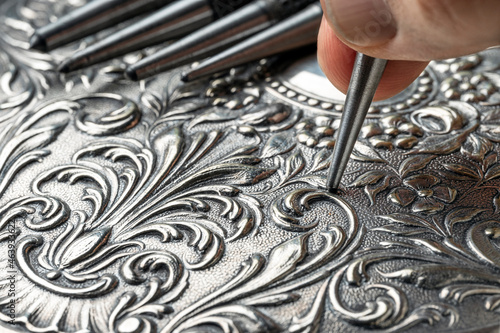 CLOSEUP OF CRAFTSMAN'S HAND EMBOSSING METAL WITH PUNCH. GOLDSMITH, SILVERSMITH, JEWELLERY AND HANDICRAFTS CONCEPT. photo