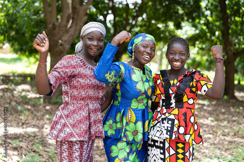 Group of young black African villagers in colourful traditional dresses smiling at the camera with their clenched fists as a symbol for women s strength and gender equality