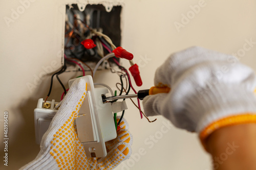 An electrician is replacing a wall switch. A DIY project concept. High voltage danger. installing wire connection using screw driver. The professional wears protective rubber gloves for safety photo