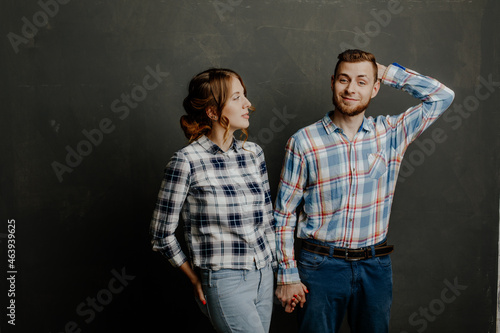 young couple in plaid shirts hugs on gray background