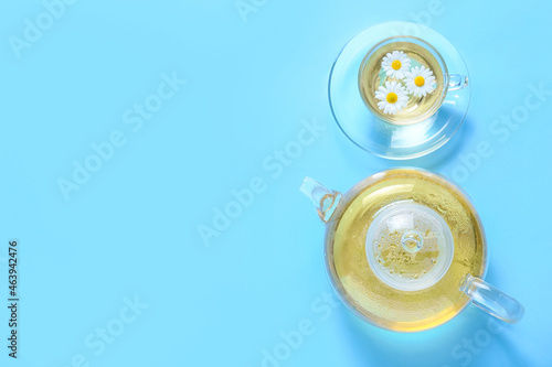 Teapot and cup of tasty chamomile tea on color background