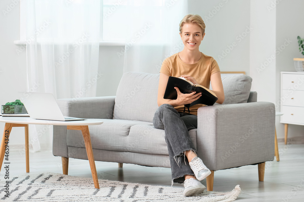 Young woman reading Holy Bible on sofa at home