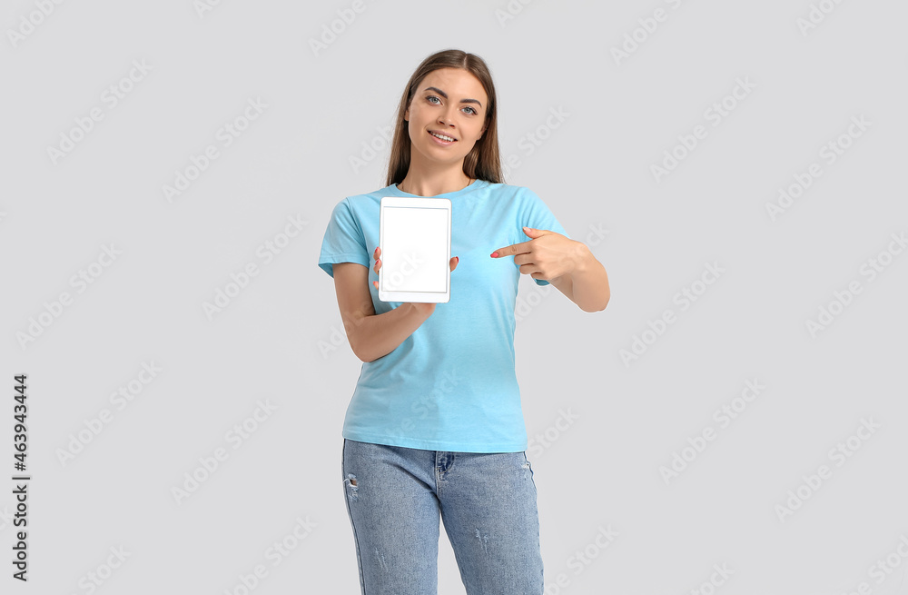 Pretty young woman pointing at tablet computer on light background Pretty young woman pointing at tablet computer on light background