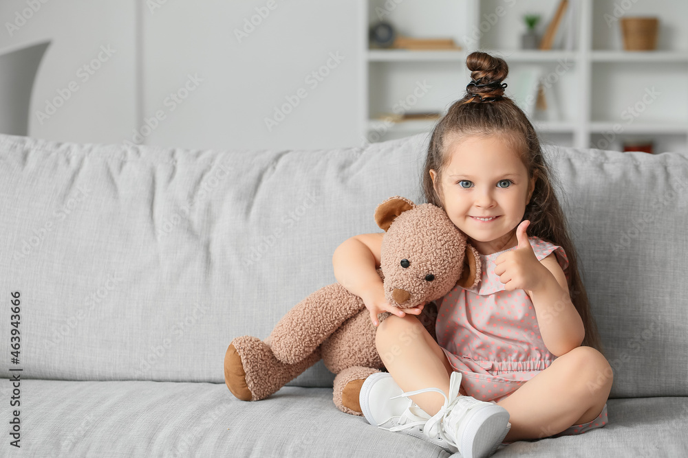Adorable little girl with teddy bear showing thumb-up at home Adorable little girl with teddy bear showing thumb-up at home