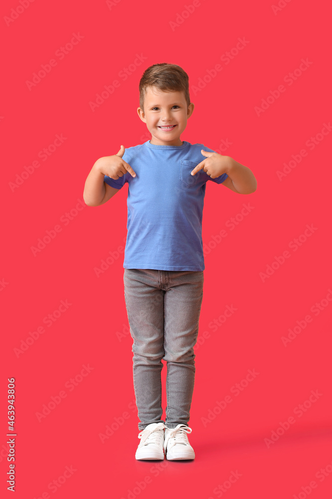 Cute little boy pointing at blue t-shirt on red background
