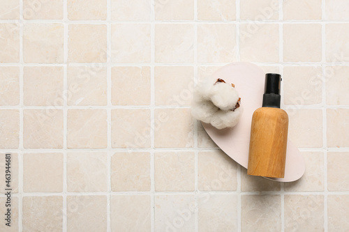 Bottle of cosmetic product and cotton flower on light tile