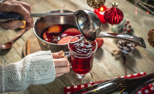 Woman is pouring fragrant hot mulled wine into a clear glass. Concept of a cozy festive atmosphere, New Year and Christmas mood