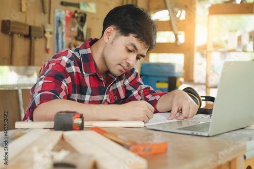 Owner entrepreneur startup small shop business. Professional of carpenter asian young man handcraft furniture making in hardwood, use laptop computer for marketing online. Factory Industry of wood.