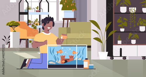 african american boy feeding fishes in aquarium domestic animal friendship with pet concept living room interior