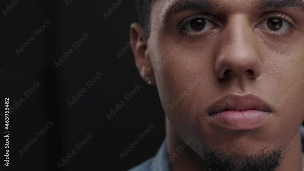 Close-up shot of young black man big eyes blinking and staring at camera. Calm portrait of handsome african american guy isolated on dark background. Slow motion. Close-up shot of young black man big eyes blinking and staring at camera. Calm portrait of handsome african american guy isolated on dark background. Slow motion.