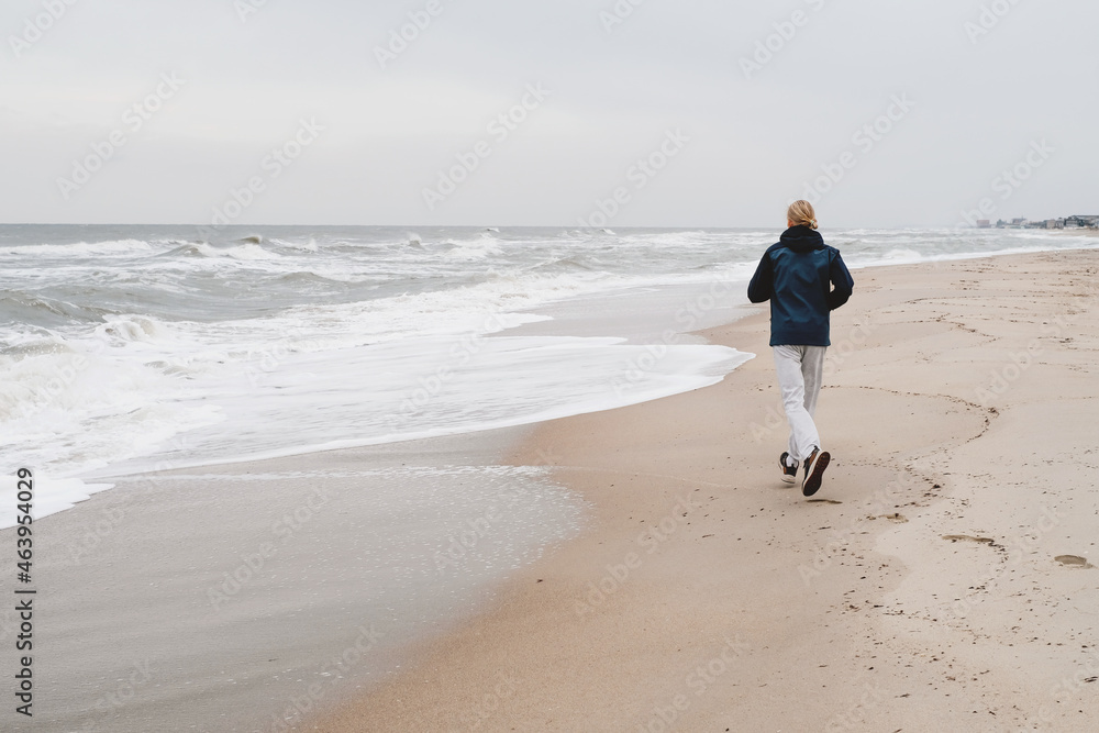 Middle age man running on the beach in autumn. Offseason rest on the sea, Healthy lifestyle. Runner athlete in warm jacket in fall by the water. Male runner training outdoors jogging in nature Middle age man running on the beach in autumn. Offseason rest on the sea, Healthy lifestyle. Runner athlete in warm jacket in fall by the water. Male runner training outdoors jogging in nature
