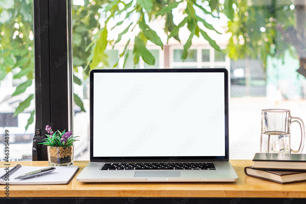 blank white screen laptop and computer screen Flower vases of plants and book objects on the table in a coffee shop front view beside the mirror blank white screen laptop and computer screen Flower vases of plants and book objects on the table in a coffee shop front view beside the mirror