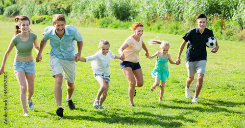 Smiling glad mother and father with four kids having fun and running on green lawn in park