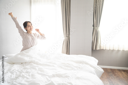 部屋の中で逆光の朝日を浴びてストレッチをする美しい日本人女性3 広角 