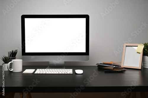 Mock up computer with blank screen, coffee cup and picture frame on black table.