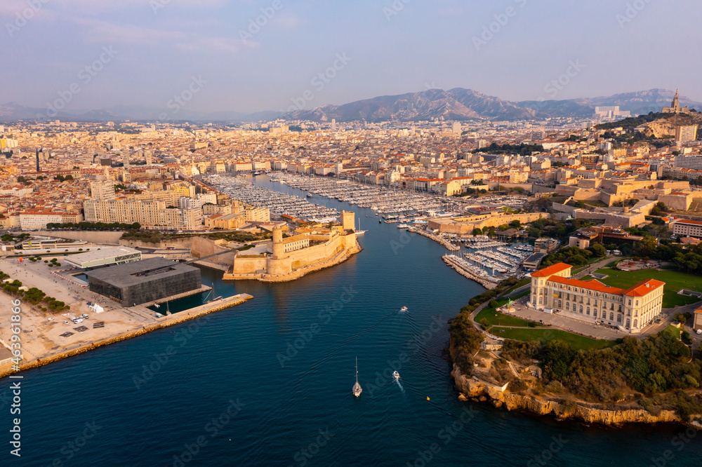 Obraz premium Picturesque drone view of modern Marseille cityscape on Mediterranean coast overlooking large Old Port with moored pleasure yachts and Fort Saint-Jean on sunny day, France