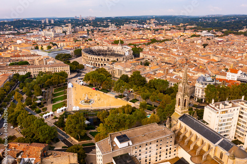 Panoramic aerial view of ancient French city of Nimes overlooking brownish tiled roofs of residential buildings in historic district and antique Arena
