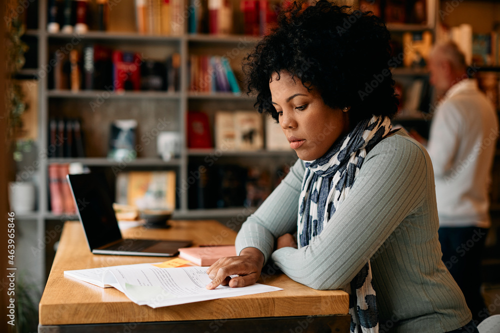 Mid adult black woman doing a research while studying in a library. Mid adult black woman doing a research while studying in a library.
