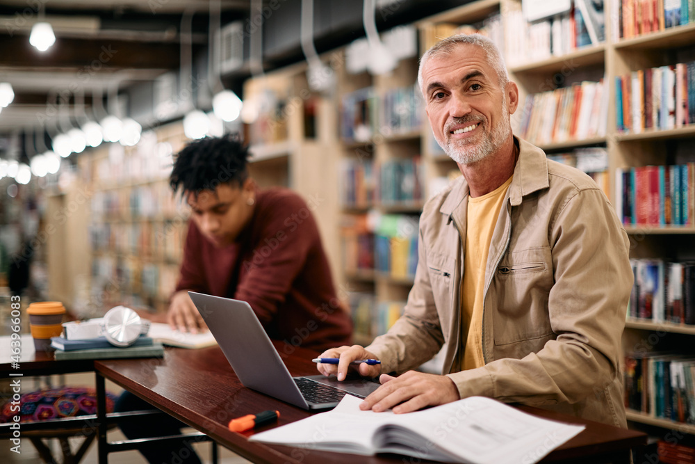 Happy mature man studying at university library and looking at camera. Happy mature man studying at university library and looking at camera.