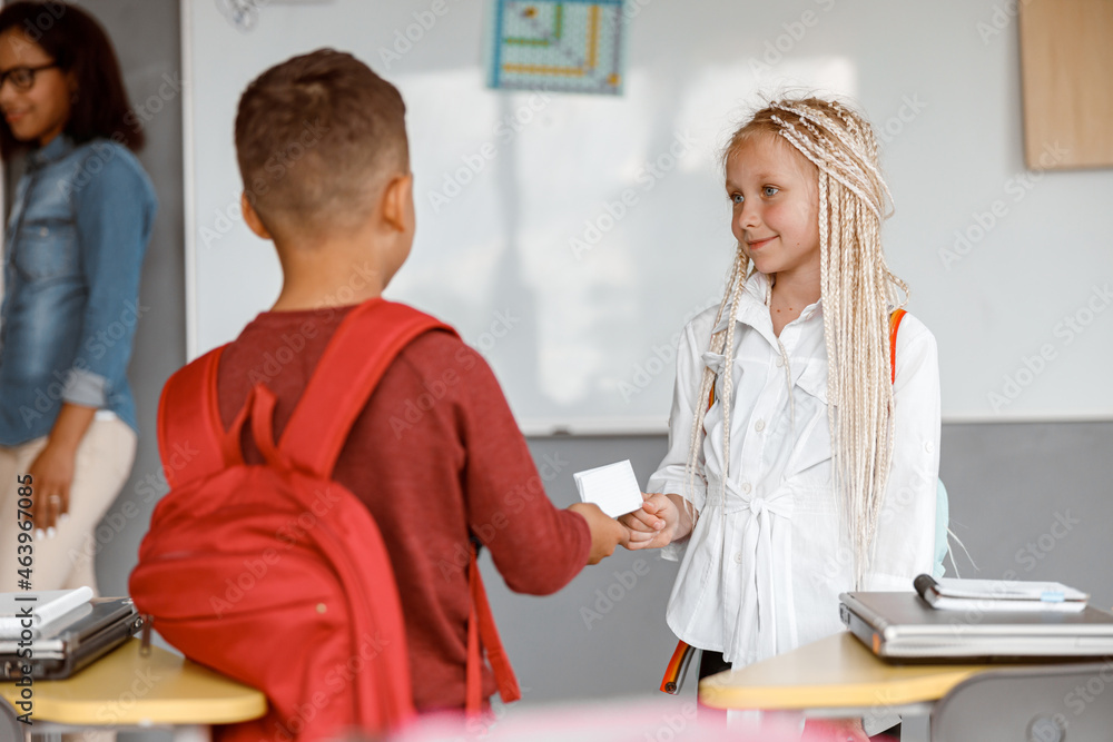 Fototapeta premium Schoolboy passing paper note to girl at school