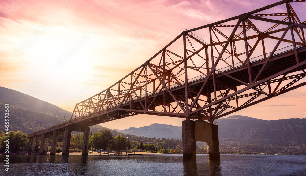 Big Orange Bridge over Kootenay River with Touristic Town in background. Sunrise Sky Art Render. Located in Nelson, British Columbia, Canada. Big Orange Bridge over Kootenay River with Touristic Town in background. Sunrise Sky Art Render. Located in Nelson, British Columbia, Canada.