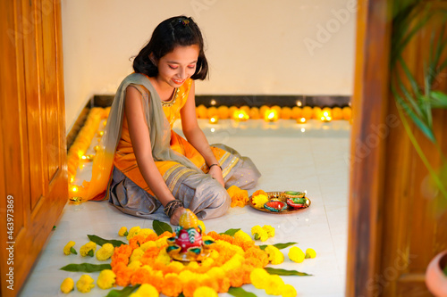 Cute indian little girl making decoration with flower and oil lamp for diwali festival at home. photo