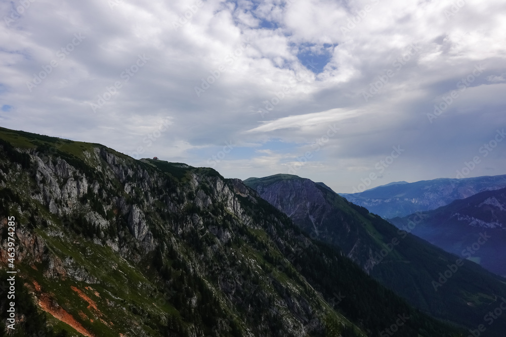 Fototapeta premium single alpine hut on the top from a huge rocky mountain with clouds