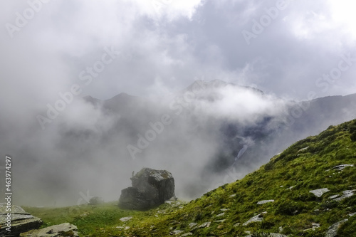 single rock on a green meadow with dense fog over high mountains